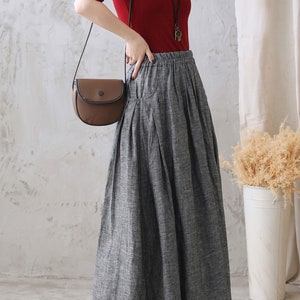May include: A gray linen skirt with a wide waistband and pleats. The skirt is long and flowy, and it is paired with a red top and a brown crossbody bag.