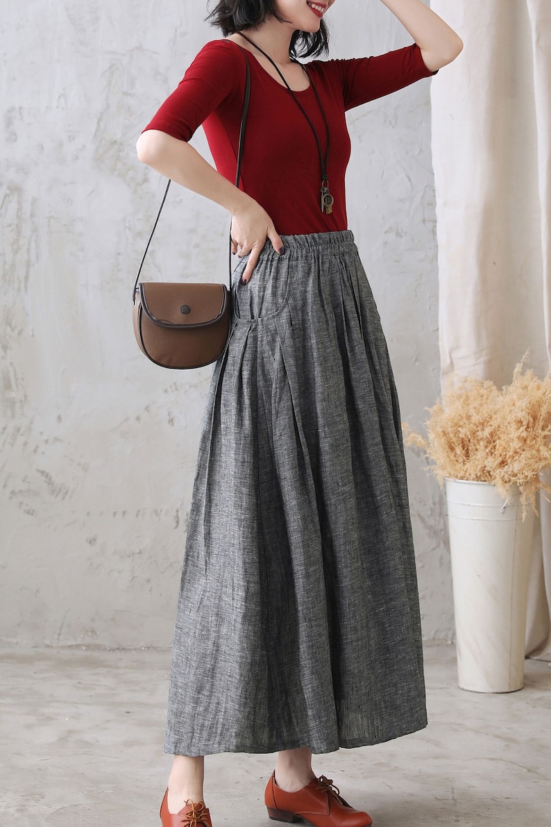 May include: A gray linen skirt with a wide waistband and pleats. The skirt is long and flowy, and it is paired with a red top and a brown crossbody bag.