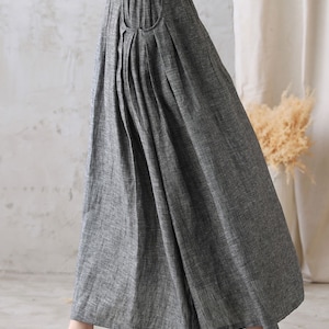 May include: A gray linen skirt with a pleated front and a single pocket on the left side. The skirt has an elastic waistband and falls to the ankles.