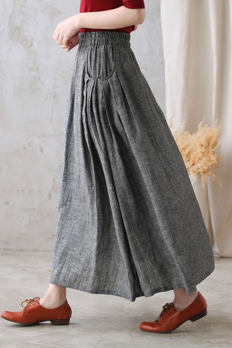 May include: A gray linen skirt with a pleated front and a single pocket on the left side. The skirt has an elastic waistband and falls to the ankles.