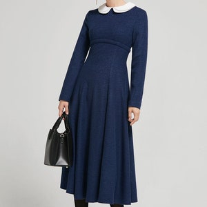Puede incluir: Un vestido midi azul marino con cuello blanco de Peter Pan y mangas largas. El vestido tiene un corpi&ntilde;o ajustado y una falda acampanada.