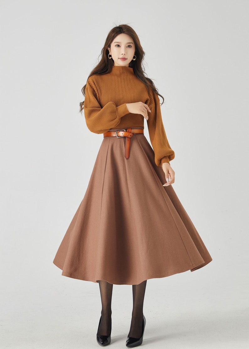 May include: A brown turtleneck sweater with long sleeves and a brown midi skirt with a brown leather belt. The woman is wearing black tights and black heels.
