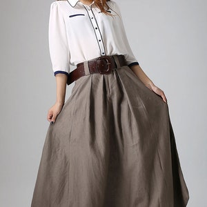 May include: A brown linen skirt with a wide brown leather belt and a silver buckle. The skirt is pleated and has a long, flowing silhouette.