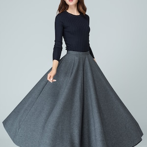 Op de afbeelding: Een vrouw draagt een zwarte longsleeve trui en een grijze, lange, ronde rok. Ze draagt zwarte hakken.