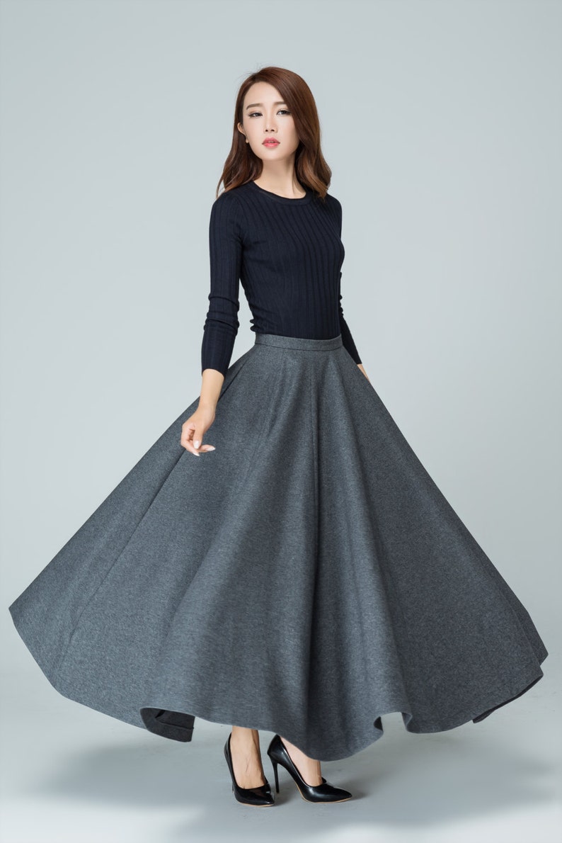 Op de afbeelding: Een vrouw draagt een zwarte longsleeve trui en een grijze, lange, ronde rok. Ze draagt zwarte hakken.