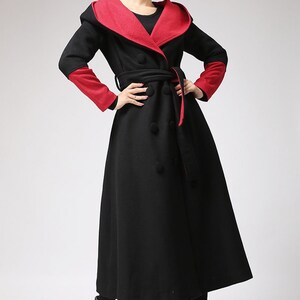 May include: A long black coat with a red lining and a hood. The coat has a double-breasted closure and a belt.