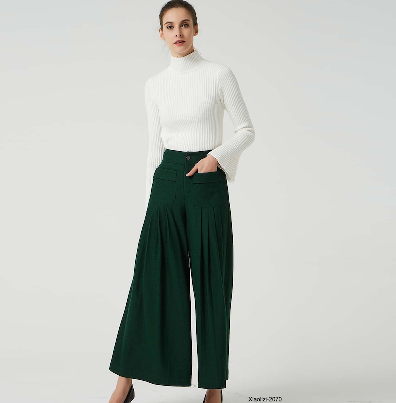 May include: A woman is wearing a white turtleneck sweater and dark green wide-leg trousers with pleats. The trousers have a high waist and pockets.