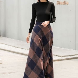 May include: A woman wearing a black long-sleeved shirt and a brown and blue plaid skirt. She is wearing a brown hat and black boots. The skirt is a maxi skirt and falls to her ankles.
