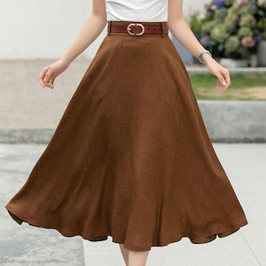 May include: A brown linen midi skirt with a brown leather belt. The skirt has a high waist and a flared silhouette.