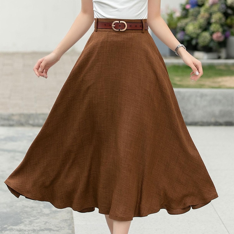 May include: A brown linen midi skirt with a brown leather belt. The skirt has a high waist and a flared silhouette.