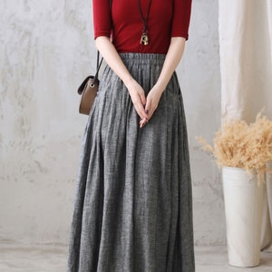 May include: A gray linen skirt with a red top and a brown leather bag. The skirt has a high waist and a flowy silhouette. The top is a simple, fitted style with short sleeves. The bag is a small, crossbody style.