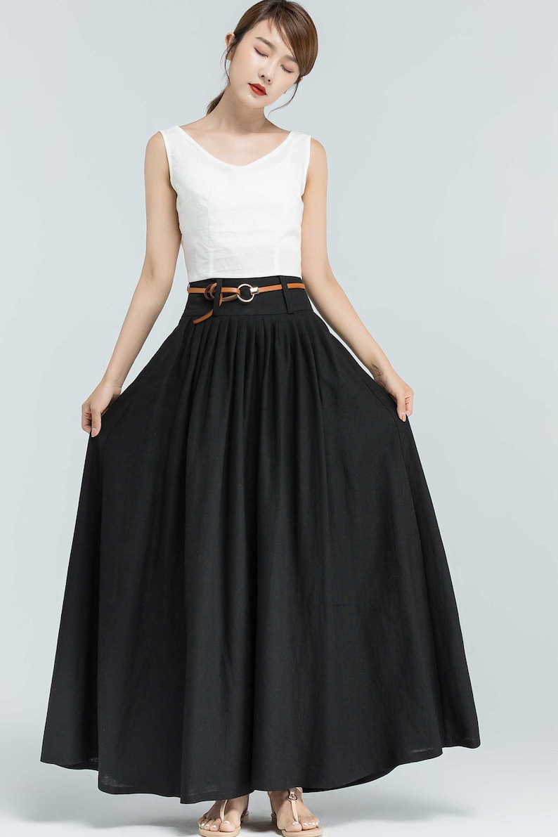 May include: A black maxi skirt with a brown belt and a gold buckle. The skirt has pleats and is made of a lightweight fabric.