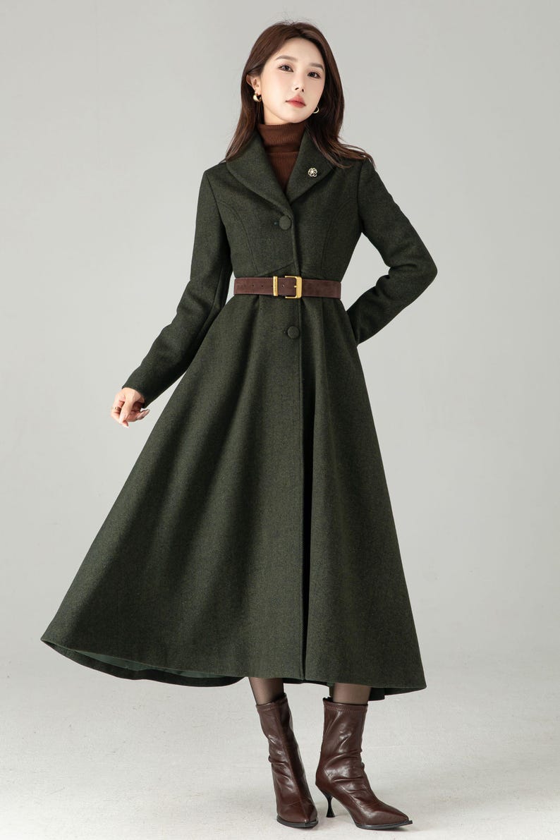May include: A dark green, long coat with a flared skirt and a brown belt. The coat has a button-down front and a notched collar. The model is wearing brown boots. The coat is a classic style, suitable for fall or winter.