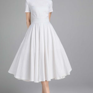 May include: A white, knee-length, A-line dress with a boat neck and short sleeves. The dress has a fitted bodice and a full skirt.