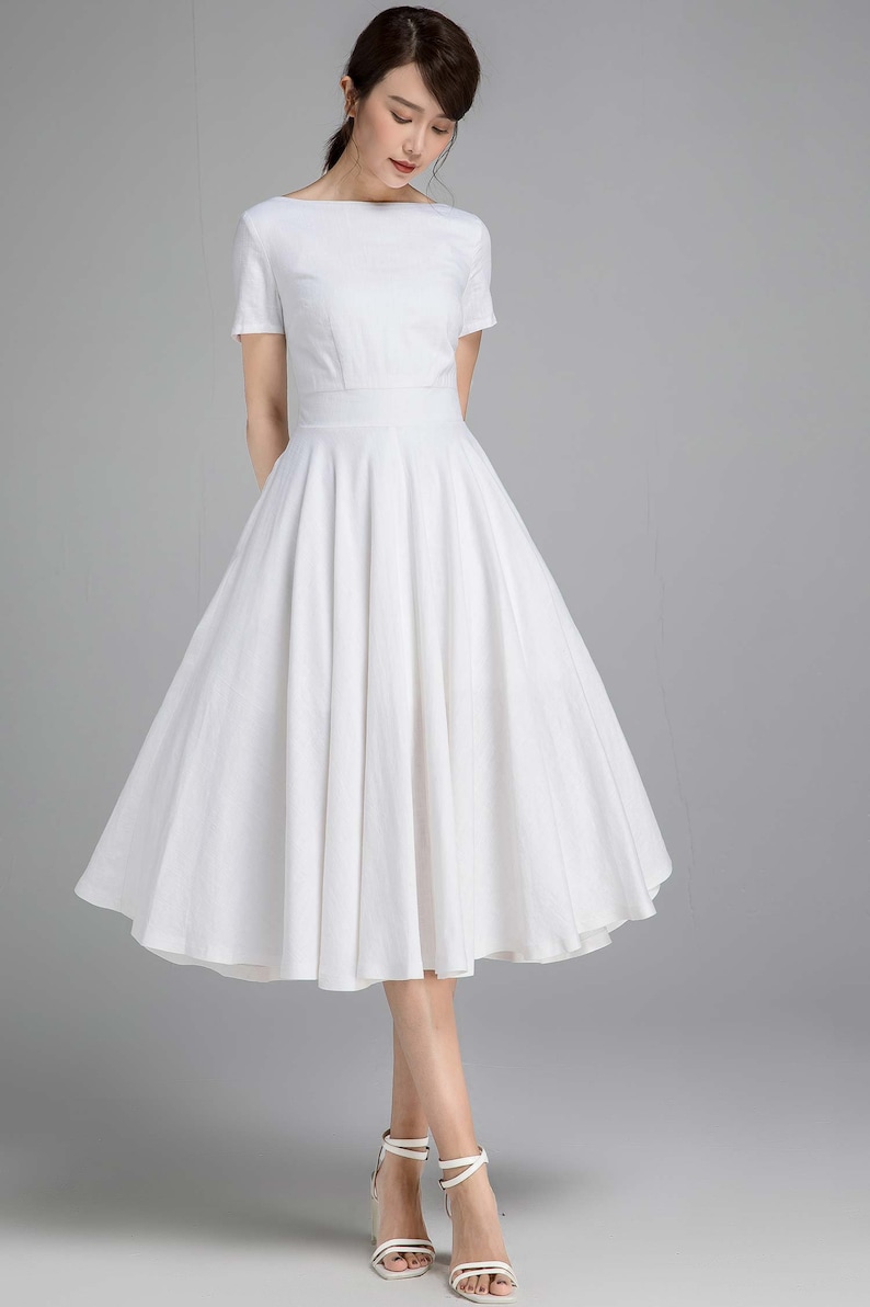 May include: A white, knee-length, A-line dress with a boat neck and short sleeves. The dress has a fitted bodice and a full skirt.