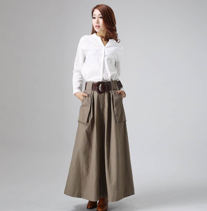 May include: A long brown skirt with a wide brown belt and large pockets. The skirt is made of a textured fabric and has a flowing silhouette.