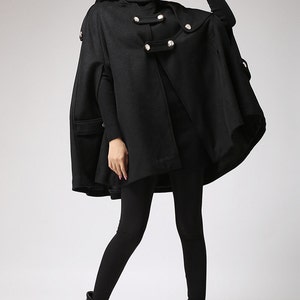 May include: A black hooded cape with a double breasted button closure and pockets. The cape is made of a soft, warm fabric and has a relaxed fit.