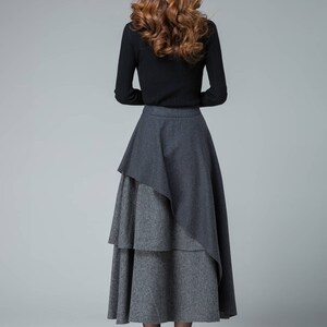 May include: A black long-sleeved shirt with a layered gray and black skirt. The skirt has a unique asymmetrical design with a longer layer in the back.