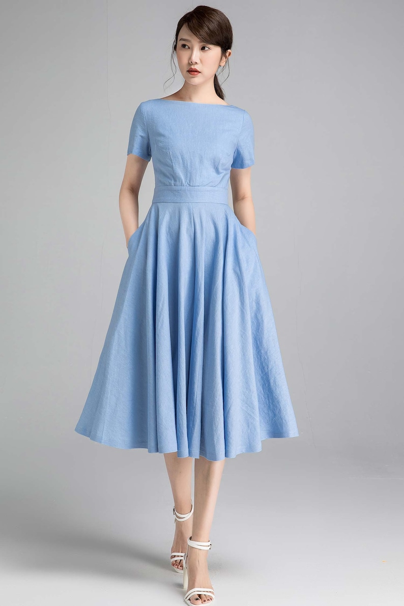 May include: A light blue midi dress with a boat neck and short sleeves. The dress has a fitted bodice and a full skirt with pockets.