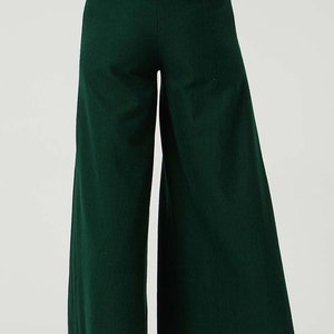 May include: A pair of wide-leg trousers in a dark green colour. The trousers have a high waist and a relaxed fit.