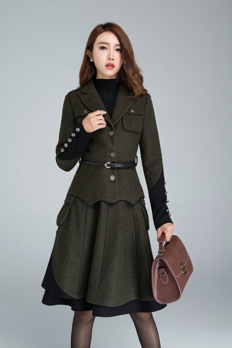Puede incluir: Una chaqueta de lana verde con un cintur&oacute;n negro y una falda negra y verde. La chaqueta tiene cierre de botones y bolsillos. La falda tiene un dise&ntilde;o en capas y un forro negro.
