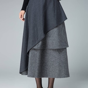 May include: A gray midi skirt with a layered design. The top layer is a solid gray, while the bottom layer is a gray and white plaid. The skirt is knee-length and has a fitted waist.