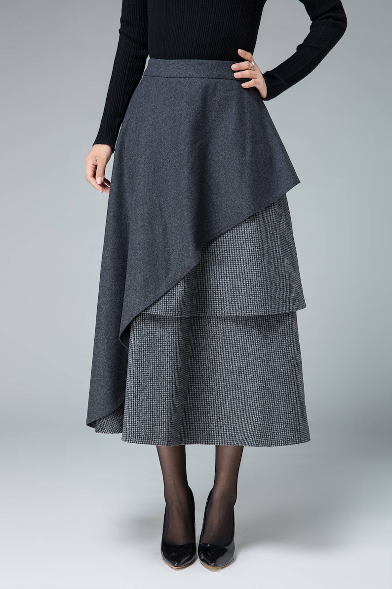 May include: A gray midi skirt with a layered design. The top layer is a solid gray, while the bottom layer is a gray and white plaid. The skirt is knee-length and has a fitted waist.