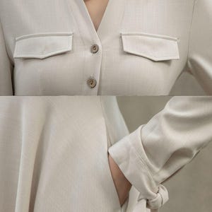 May include: A beige linen dress with a collared neckline, long sleeves, and a button-up front. The dress has two flap pockets on the chest and a tie detail at the cuffs.