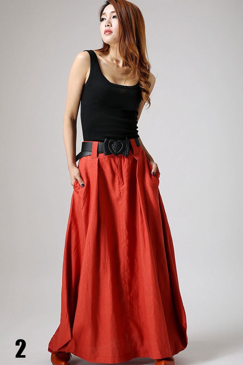 May include: A red maxi skirt with a black belt featuring a heart-shaped buckle. The skirt has a pleated design and pockets on the sides.