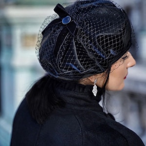 May include: A black velvet beret with a black mesh veil. The beret has a black button on the side.