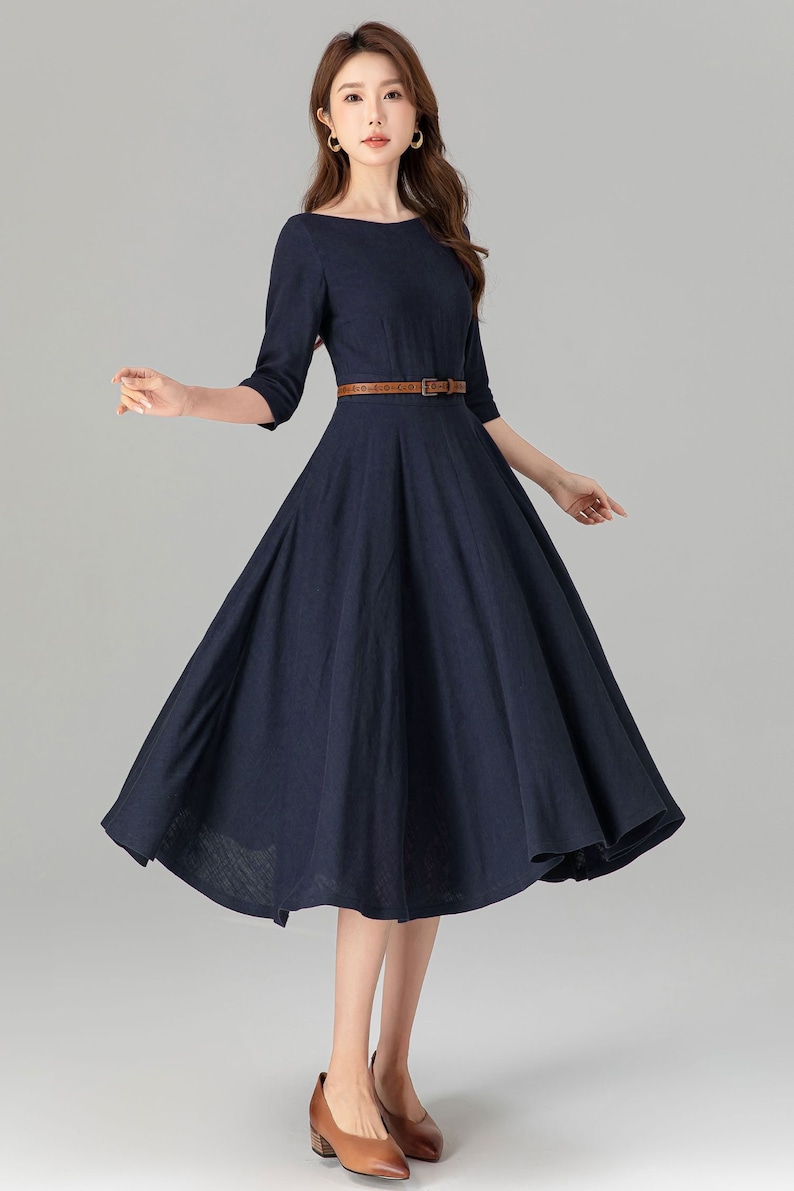 May include: A navy blue midi dress with a brown belt. The dress has a round neckline and 3/4 sleeves. The dress is made of a soft, comfortable fabric.