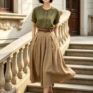 May include: A woman wearing a green short-sleeved button-down shirt, a brown skirt, and a brown belt. She is also wearing a brown hat and black sandals. The outfit is suitable for a casual or semi-formal occasion.