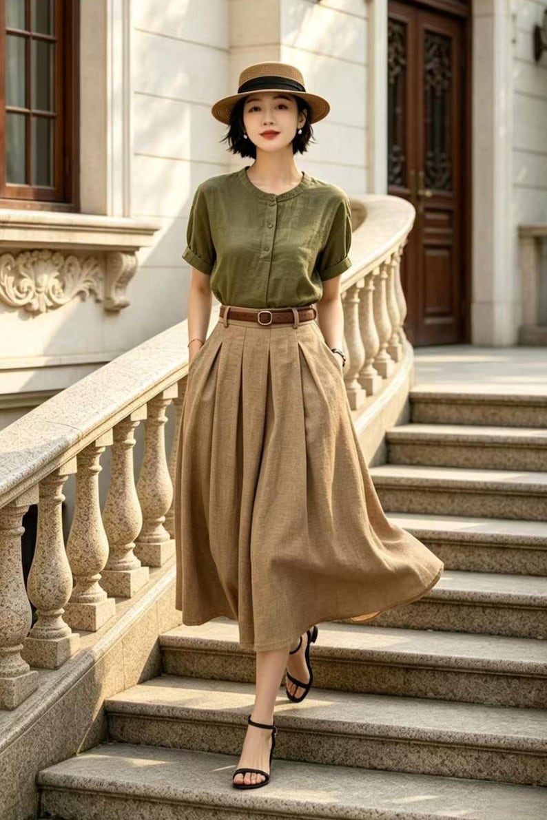 May include: A woman wearing a green short-sleeved button-down shirt, a brown skirt, and a brown belt. She is also wearing a brown hat and black sandals. The outfit is suitable for a casual or semi-formal occasion.