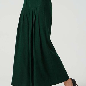 May include: A dark green wide-leg trouser with pleats and a single button fastening at the waist. The trouser has a large patch pocket on the front.