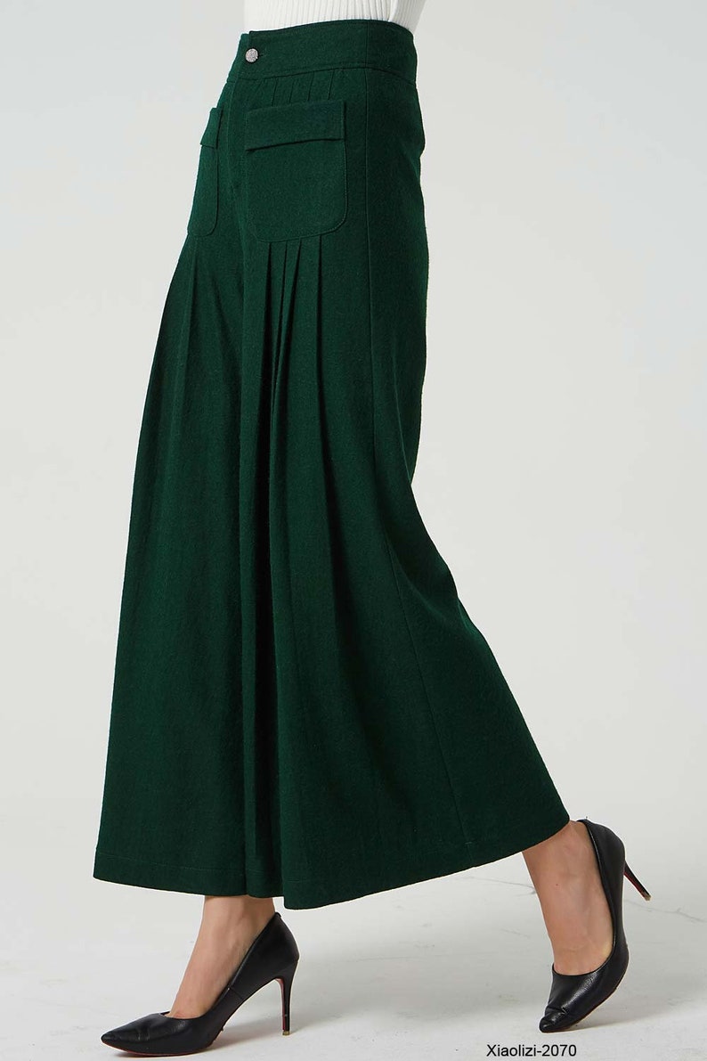 May include: A dark green wide-leg trouser with pleats and a single button fastening at the waist. The trouser has a large patch pocket on the front.