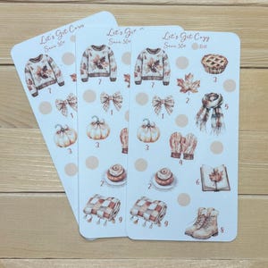 Puede incluir: Tres hojas de pegatinas con ilustraciones de temática otoñal. Cada hoja presenta un suéter, un lazo, una calabaza, una tarta, una hoja de arce, una bufanda, guantes, un rollo de canela, una manta y botas. El texto "Let's Get Cozy" y "Save 50+" es visible.
