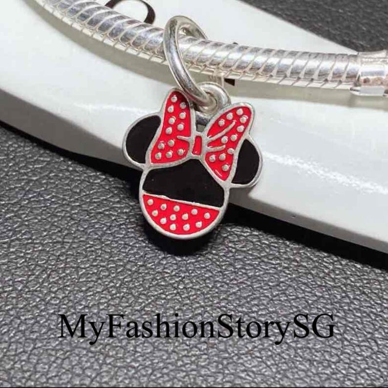 May include: A silver charm shaped like a mouse head with a red and white polka dot bow and black enamel details, attached to a silver snake chain bracelet. The text MyFashionStorySG is visible at the bottom of the image.