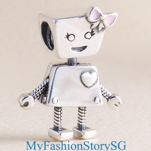 May include: A silver robot charm with a pink bow on its head and a heart on its chest. The robot has a smiling face and articulated arms and legs. The charm is a pendant or bead.