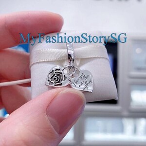 May include: A silver charm with two heart pendants. One heart features a rose design, and the other has the inscription "I love you more than anything." The charm is attached to a silver bail.