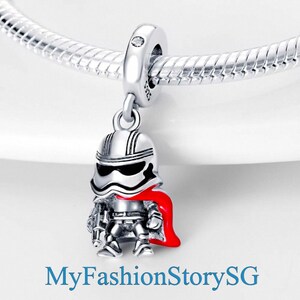 Könnte beinhalten: Ein silberner Charm-Anhänger mit einem Stormtrooper mit rotem Umhang, befestigt an einem silbernen Armband. Der Stormtrooper hat ein schwarzes Visier und hält einen Blaster. Ein Sammlerstück für Fans.