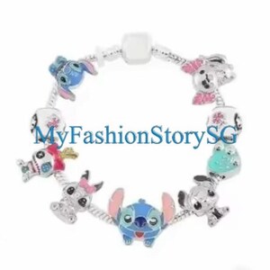 May include: A silver charm bracelet featuring colorful cartoon character charms. The bracelet includes blue, pink, and white charms with the text "MyFashionStorySG". The charms are in the shape of cartoon characters.