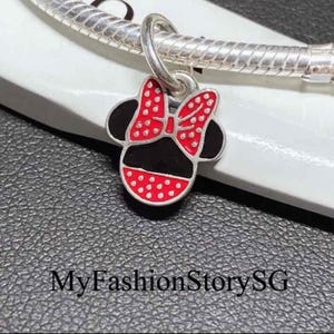 May include: A silver charm shaped like a mouse head with a red and white polka dot bow and black enamel details, attached to a silver snake chain bracelet. The text MyFashionStorySG is visible at the bottom of the image.