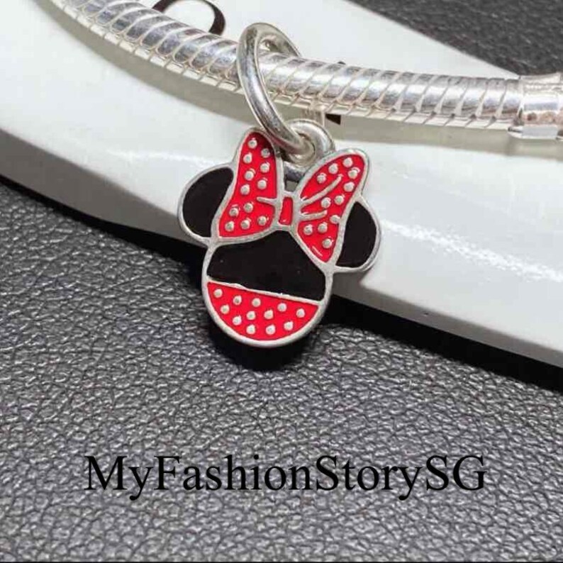 May include: A silver charm shaped like a mouse head with a red and white polka dot bow and black enamel details, attached to a silver snake chain bracelet. The text MyFashionStorySG is visible at the bottom of the image.