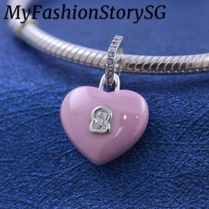 May include: A pink heart-shaped charm with a keyhole design. The charm is suspended from a silver-colored chain. The text "MyFashionStorySG" is at the top of the image.