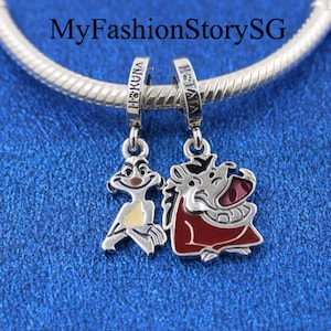 May include: Two silver charm bracelets with a silver charm of Timon and Pumbaa from Disney's The Lion King. The charms are attached to the bracelets with a silver loop. The charms are both enamelled with red, yellow, and brown paint. The charms have the words "Hakuna Matata" and "Hakuna" engraved on them.