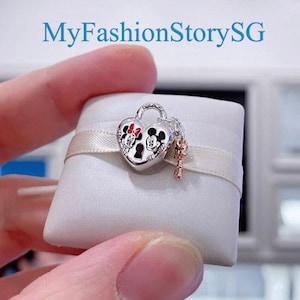 May include: A silver charm in the shape of a heart lock with Mickey and Minnie Mouse on it. The charm has a small key attached to it.