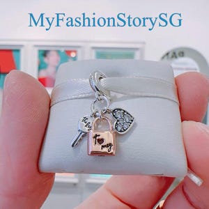 May include: A silver charm with a rose gold padlock, a silver key, and a silver heart with clear cubic zirconia stones. The charm is in a white velvet pouch. The padlock has the words "to my" engraved on it. The key has the words "this key" engraved on it.