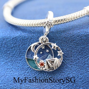 Puede incluir: Un charm de plata con un diseño de esmalte azul y verde que representa un campamento bajo un cielo estrellado. El charm incluye una luna creciente, estrellas, una tienda de campaña y una fogata.