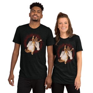 Può includere: T-shirt grigio scuro con grafica di un gatto arancione e bianco tenuto da due mani, circondato da un design a scoppio rosso. Le magliette sono indossate da un uomo e una donna.