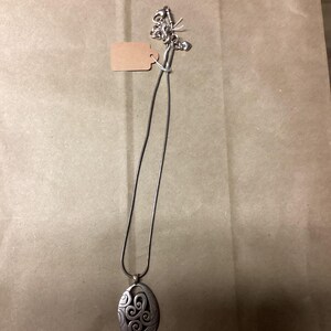 Puede incluir: Un collar de plata con un colgante con un dise&ntilde;o de espiral. El colgante es de forma ovalada y cuelga de una fina cadena de plata.